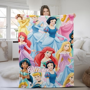 Pu&ograve; includere: Una morbida coperta in pile con un collage colorato di varie principesse animate nei loro abiti caratteristici, inclusi personaggi con capelli rossi, biondi e scuri. Il nome Olivia &egrave; stampato in un corsivo bianco al centro della coperta.