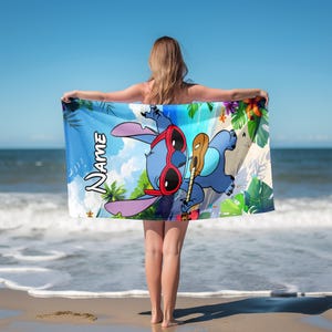 May include: A blue beach towel featuring a cartoon character wearing red sunglasses and holding a ukulele. The towel has a tropical scene with palm trees, flowers, and the word "Name" in white. The background shows the ocean and sky.