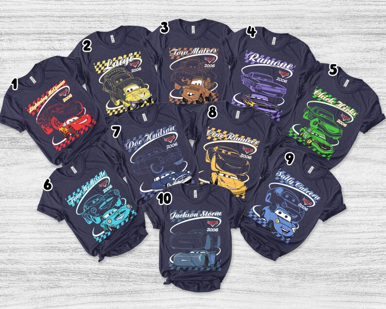 Peut inclure: Une collection de dix t-shirts bleu marine &agrave; manches courtes, chacun arborant un personnage du film Cars. Les motifs incluent Lightning McQueen, Luigi, Tow Mater, Ramone, Chick Hicks, Finn McMissile, Doc Hudson, Cruz Ramirez, Sally Carrera et Jackson Storm, tous accompagn&eacute;s de leurs noms et de l'ann&eacute;e 2006.