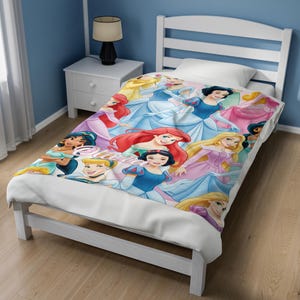 Pu&ograve; includere: Una coperta da letto bianca con una stampa grafica colorata di varie principesse animate, tra cui Biancaneve, Ariel e Cenerentola, con il nome Olivia scritto in un carattere corsivo bianco al centro del design del tessuto.