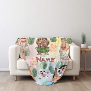 Puede incluir: Una colorida manta con ilustraciones de personajes de una popular pel&iacute;cula animada. El dise&ntilde;o incluye personajes, flores tropicales y la palabra "Name" en rojo. La manta est&aacute; sobre un sof&aacute; blanco.