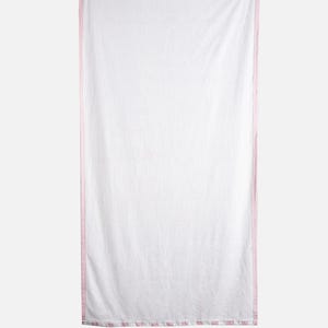 May include: White rectangular beach towel with a pink and white striped border. The towel is hanging vertically against a light gray background. The towel is made of a soft, lightweight material.
