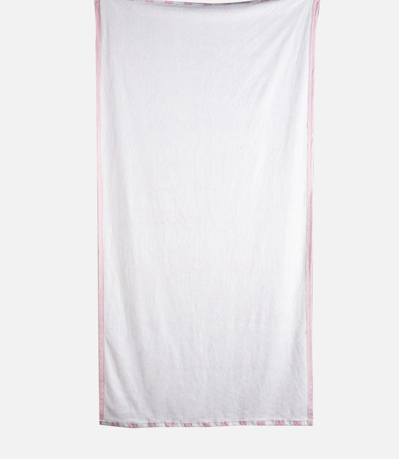 May include: White rectangular beach towel with a pink and white striped border. The towel is hanging vertically against a light gray background. The towel is made of a soft, lightweight material.