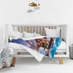 May include: A white crib featuring a blanket printed with a scene of a character holding a large hook in a boat on blue ocean water, accompanied by a small pig character. A mobile with gold and gray clouds and stars hangs above the white crib.