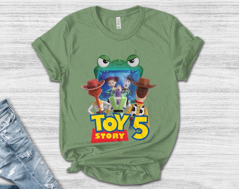 May include: Green t-shirt featuring a graphic of characters from the movie Toy Story 5. The design includes Woody, Buzz Lightyear, and Jessie, with the words "Toy Story 5" in a colorful font. The shirt is made of a soft material.