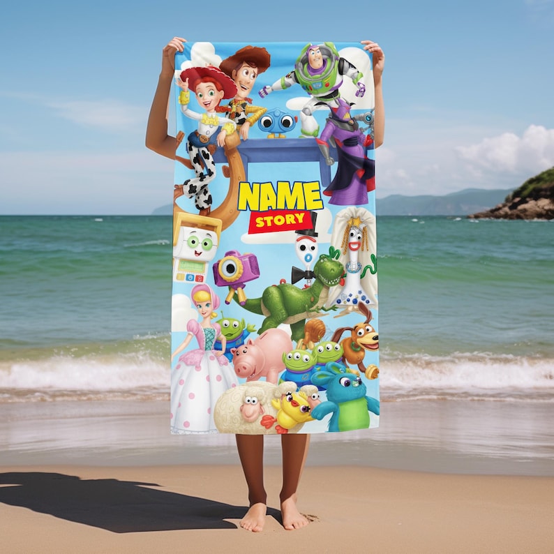 May include: A rectangular beach towel featuring a colorful collage of various animated characters from the Toy Story franchise. The design includes the text NAME STORY in yellow and red letters against a light blue background with clouds.
