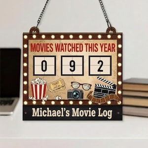 May include: Wooden movie log sign with the text "MOVIES WATCHED THIS YEAR" and the number "092". The sign includes illustrations of popcorn, movie tickets, glasses, a camera, and a film clapper. The name "Michael's Movie Log" is displayed at the bottom.