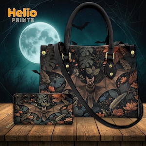 May include: A black handbag and matching wallet featuring a bat design with botanical elements. The bat is centered on both items, with a full moon and bats in the background. The bag has a top handle and a shoulder strap.
