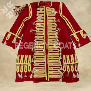 Puede incluir: Un abrigo rojo con ribetes y borlas doradas. El abrigo presenta un cuello alto, filas de botones dorados y adornos dorados decorativos en las mangas y la parte delantera. El texto "REGENCY COATS" es visible.