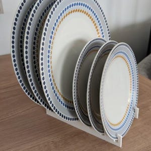 May include: Set of five white ceramic plates with a blue and gold geometric pattern. The plates are stacked on a white stand.