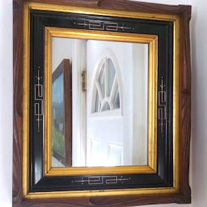 May include: A vintage wood framed mirror with a black and gold inner frame. The inner frame has a geometric design in gold.