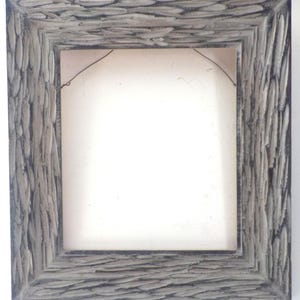 May include: A rectangular picture frame with a textured, gray finish. The frame has a light gray interior and a dark gray exterior. A wire is strung across the back for hanging. The frame is empty.