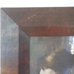 K&ouml;nnte beinhalten: Ein dunkelbrauner Holzbildrahmen mit einem verblassten Bild einer Person darin. Der Rahmen hat ein schlichtes Design mit einem leicht erh&ouml;hten Rand.