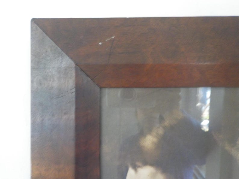 K&ouml;nnte beinhalten: Ein dunkelbrauner Holzbildrahmen mit einem verblassten Bild einer Person darin. Der Rahmen hat ein schlichtes Design mit einem leicht erh&ouml;hten Rand.