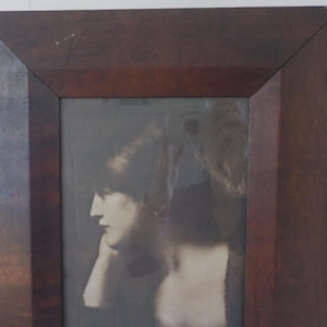 K&ouml;nnte beinhalten: Ein Schwarzwei&szlig;-Foto aus der Zeit, das eine Frau mit kurzen Haaren zeigt, die ein helles Kleid tr&auml;gt. Das Foto ist in einem dunklen Holzrahmen gerahmt.