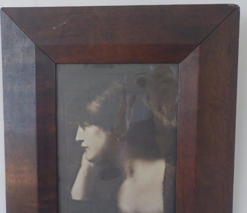 K&ouml;nnte beinhalten: Ein Schwarzwei&szlig;-Foto aus der Zeit, das eine Frau mit kurzen Haaren zeigt, die ein helles Kleid tr&auml;gt. Das Foto ist in einem dunklen Holzrahmen gerahmt.