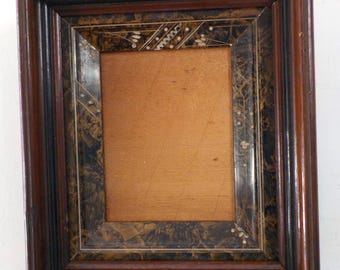 May include: A rectangular wooden picture frame with a dark brown finish. The frame has a decorative inner border with a black and gold pattern and small white accents. The interior of the frame is a light brown color.