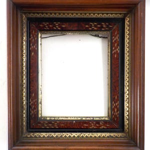 May include: A rectangular wooden picture frame with a dark brown finish. The frame has a layered design with gold and black accents. The inner frame has a reddish-brown pattern. The center is empty.