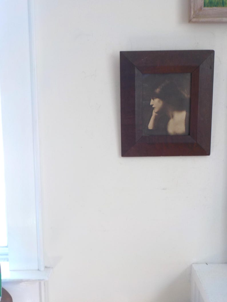 K&ouml;nnte beinhalten: Ein gerahmtes Schwarzwei&szlig;foto einer Frau mit dunklen Haaren, die zur Seite schaut und ihr Kinn auf ihrer Hand ruht.