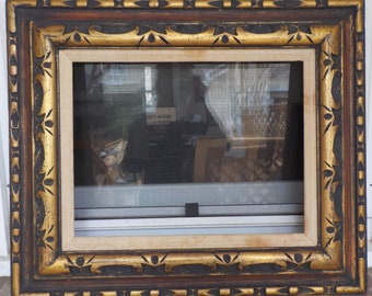 May include: A gold and black ornate picture frame with a decorative carved design. The frame is made of wood and has a distressed finish.