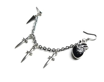 May include: A silver-toned earring set featuring a chain with three small dagger charms and a single black heart charm. The earring has a post and hook closure, with a dagger stud and a heart-shaped charm.