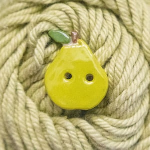 May include: A pear-shaped button with a glossy yellow finish, featuring a small green leaf and a brown stem at the top. The button has two circular holes in the centre for attachment, showcasing a smooth, reflective surface texture throughout.