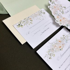 May include: A set of white wedding stationery including an RSVP card with the text Kindly respond by December 12, 2025, an accommodation card, and a die-cut invitation card, all featuring floral illustrations in soft peach, cream, and green tones.