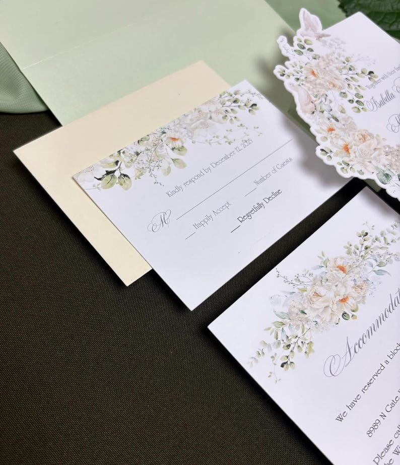May include: A set of white wedding stationery including an RSVP card with the text Kindly respond by December 12, 2025, an accommodation card, and a die-cut invitation card, all featuring floral illustrations in soft peach, cream, and green tones.