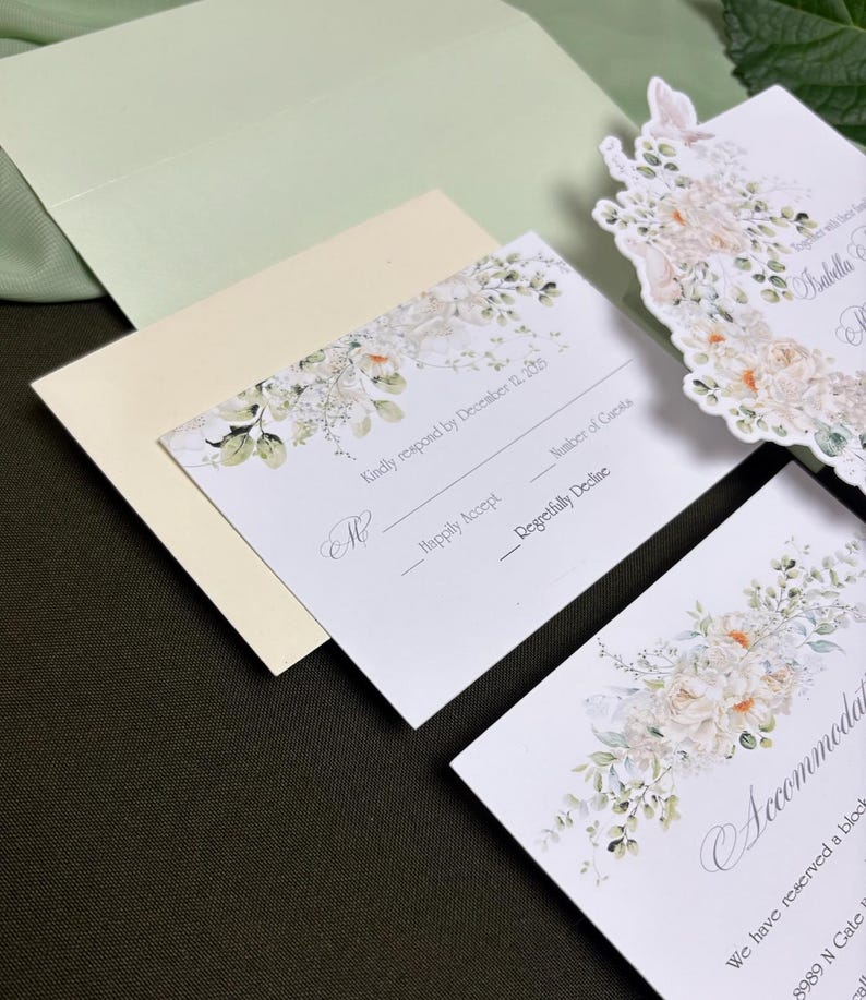 May include: A wedding stationery set featuring white cards with floral illustrations in soft peach and green tones. The response card includes the text Kindly respond by December 12, 2025, Happily Accept, and Regretfully Decline, alongside a pale green envelope.