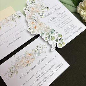 May include: A wedding invitation suite featuring white cardstock with floral and eucalyptus illustrations. The text includes names Isabella Morgan and Michael Winston, date January 24, 2025, and location Flying Horse Resort, Colorado Springs.