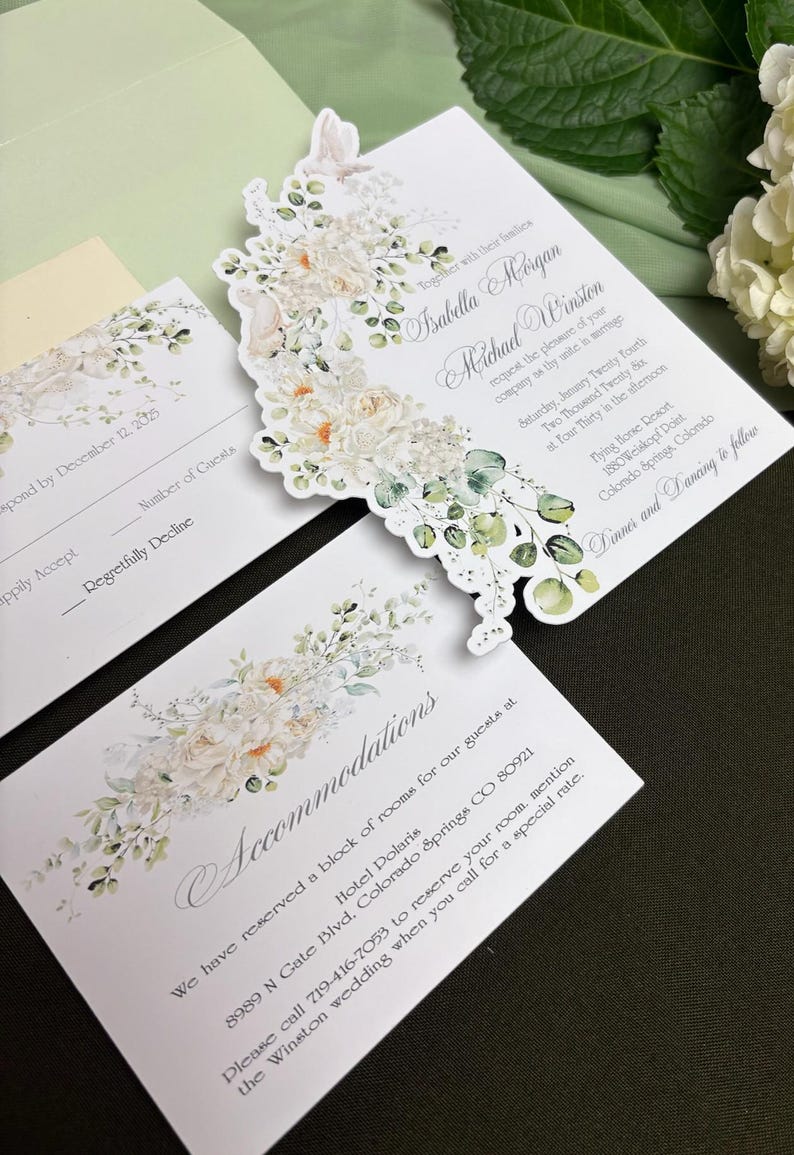 May include: A wedding invitation suite featuring white cardstock with floral and eucalyptus illustrations. The text includes names Isabella Morgan and Michael Winston, date January 24, 2025, and location Flying Horse Resort, Colorado Springs.