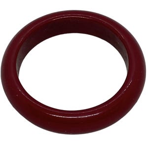 Könnte beinhalten: Ein massives, weinrotes Armreif-Armband. Das kreisförmige Armband besteht aus einem glatten, glänzenden Material. Das Schmuckstück ist ein schlichtes, klassisches Design.