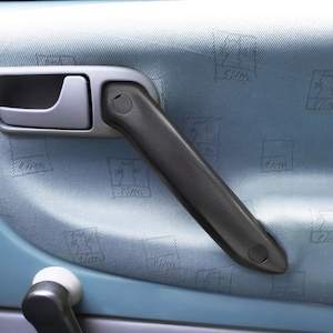 Op de afbeelding: Close-up van een auto-interieur. De afbeelding toont een grijze deurgreep en een zwarte deurtrekker. Het deurpaneel is lichtblauw met een subtiel patroon.