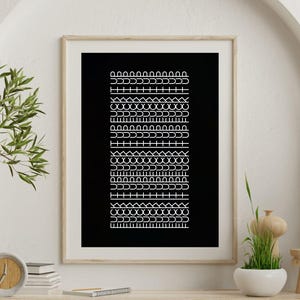 May include: A framed art print with a black backdrop and a series of white geometric patterns. The patterns include arches, lines, and other shapes. The frame is light wood, and the artwork is displayed on a wooden shelf.
