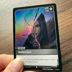Peut inclure: Une carte de jeu rectangulaire intitulée Reflection présentant un effet de verre brisé holographique sur une illustration d'un personnage aux cheveux sombres et aux yeux jaunes, portant un doigt à ses lèvres. La carte inclut une valeur d'attaque zéro.