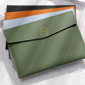 May include: A stack of leather-like document holders in various colors: green, light blue, orange, and black. The green holder is in the foreground, with a gold emblem featuring the letters "P" and "R". The holders have a simple, clean design.