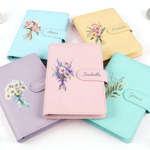 Puede incluir: Cinco diarios personalizados y coloridos con diseños florales. Cada diario presenta un color diferente: azul claro, lavanda, rosa, amarillo y turquesa. Los diarios tienen un cierre con un nombre impreso en cada uno.