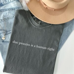 May include: A dark grey t-shirt with the text "due process is a human right" printed in white on the front.