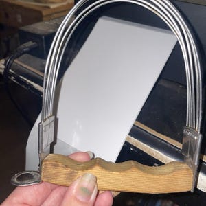 Puede incluir: Un mezclador de masa de cocina con mango de madera de agarre contorneado y cinco alambres de acero inoxidable arqueados y paralelos unidos a soportes metálicos en los extremos, diseñado para cortar mantequilla en la harina.