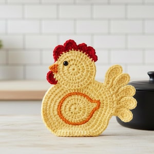 May include: A yellow crocheted chicken figure with a red comb and wattle, an orange beak, and a black eye. The body features a circular orange accent, and the tail consists of four rounded, fan-shaped crocheted segments in matching yellow yarn.