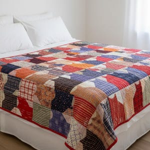 Può includere: Una trapunta patchwork con un motivo ripetitivo di sagome di gatti in varie texture e colori di tessuto, inclusi motivi rossi, blu, arancioni e a quadri. La trapunta è rifinita con un bordo rosso ed è stesa su un letto con lenzuola bianche.