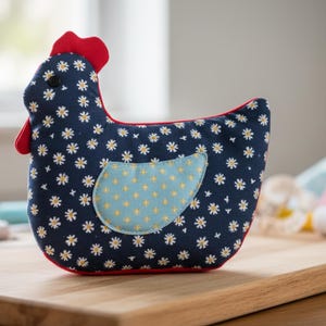 May include: A stuffed chicken-shaped decorative item. The body is navy blue with white daisy patterns, a light blue wing with yellow stars, and red accents. It is placed on a wooden cutting board.