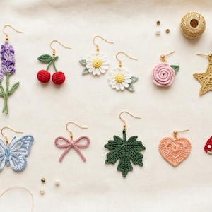 May include: A collection of ten individual crochet earrings featuring various shapes including lavender sprigs, cherries, daisies, a rose, a star, a butterfly, a bow, a leaf, a heart, and a mushroom, all attached to gold-toned metal earring hooks.