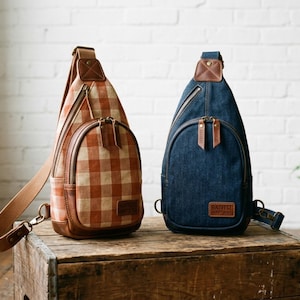 May include: Two sling backpacks with a single shoulder strap. One bag features a tan and orange gingham check pattern, while the other is solid dark blue denim. Both bags have brown leather accents, metal zippers, and a rectangular leather brand patch.