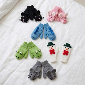 May include: A collection of children's mittens in various designs, including black cat, pink bunny, blue dinosaur, green frog, snowman, and gray mouse. The mittens are made of knitted fabric and are arranged on a white surface.