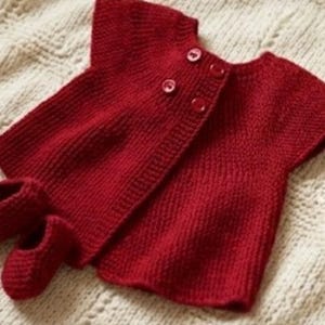 May include: A deep red knitted short-sleeved cardigan featuring four matching red buttons at the upper chest area, accompanied by a pair of small, matching red knitted booties. The set is crafted with a consistent textured knit pattern throughout.