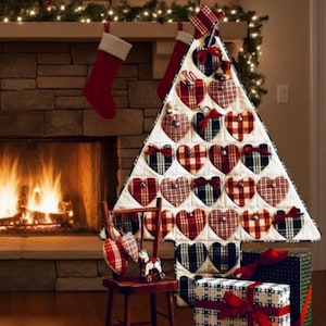 May include: A Christmas tree-shaped advent calendar made of white fabric with red, black, and white plaid hearts. The tree is decorated with small bows and sits in front of a fireplace with stockings.