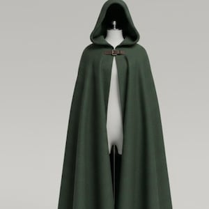 May include: A dark green hooded cloak with a brown leather clasp. The cloak is displayed on a mannequin against a neutral background. The cloak has a long, flowing design.
