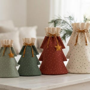 Könnte beinhalten: Vier Geschenktüten aus Stoff in Form von Weihnachtsbäumen in verschiedenen Größen. Die Tüten sind hellgrün, dunkelgrün, rostrot und cremefarben mit kleinen Sternenmustern. Jede Tüte hat einen Kordelzug mit braunem Band und einem kleinen Stern.