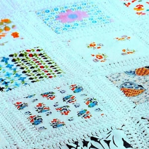 May include: A handmade quilt featuring a grid of square fabric patches joined by white crocheted borders. Each patch displays a unique floral or patterned print in various colors including orange, blue, red, and yellow on a white background.